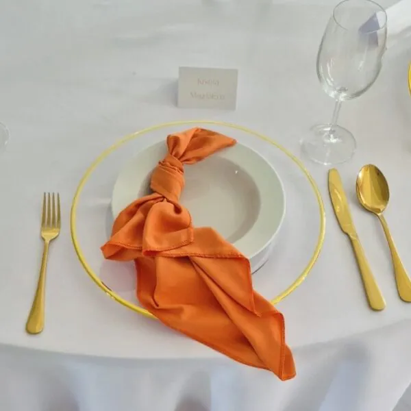 Elegantné prestieranie so zlatými príbormi a oranžovým látkovým príručníkom