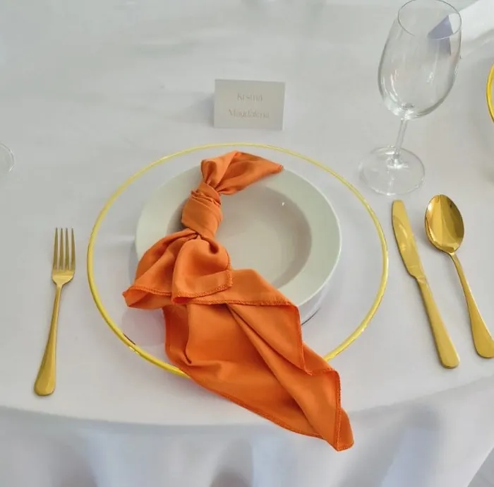 Elegantné prestieranie so zlatými príbormi a oranžovým látkovým príručníkom