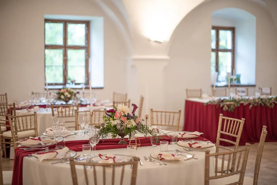 Svadobná výzdoba s červeným obrusovým behúňom a kvetinovými aranžmánmi Červený kameň