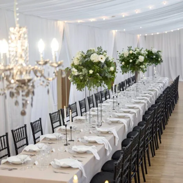 Dlhý svadobný stôl s čiernymi chiavari stoličkami a bielym obrusom
