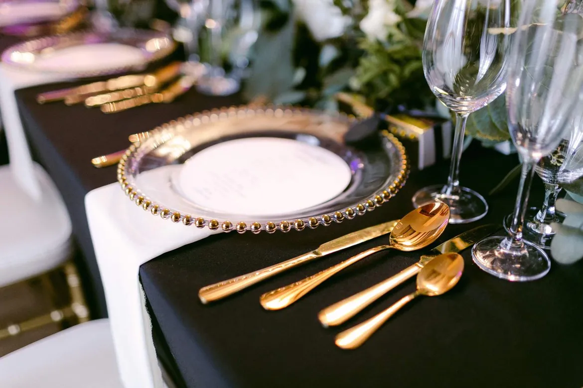 Čierne prestieranie so zlatými príbormi a skleneným klubovým tanierom s perličkami