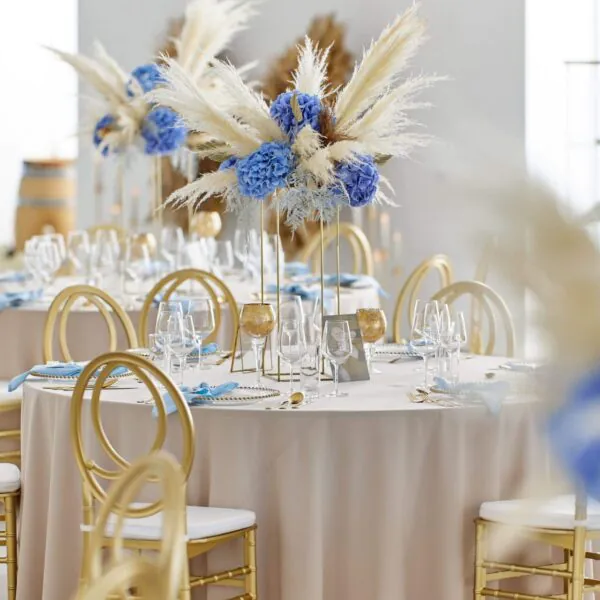 Svadobná výzdoba so zlatými stoličkami a modrými kvetinovými aranžmánmi Elesko Galéria