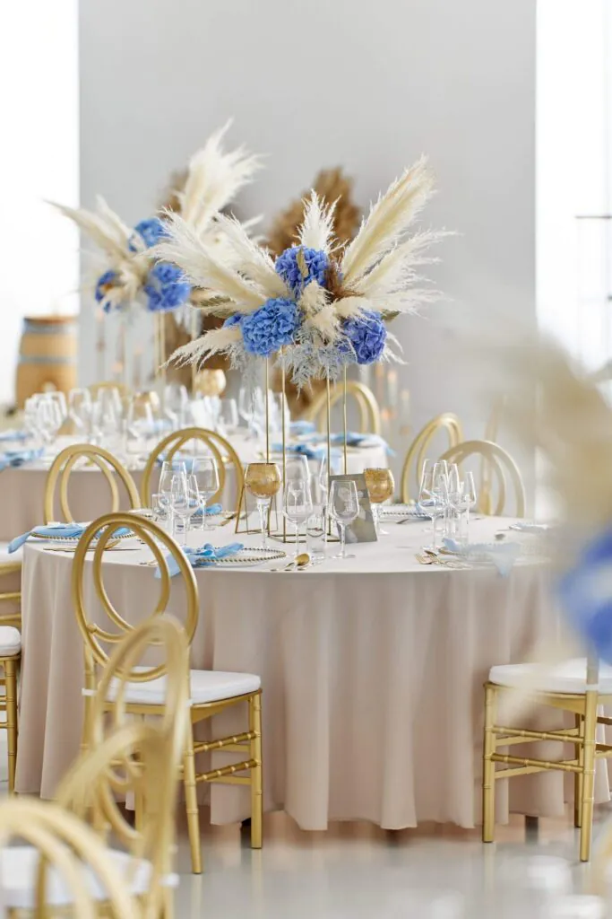 Svadobná výzdoba so zlatými stoličkami a modrými kvetinovými aranžmánmi Elesko Galéria