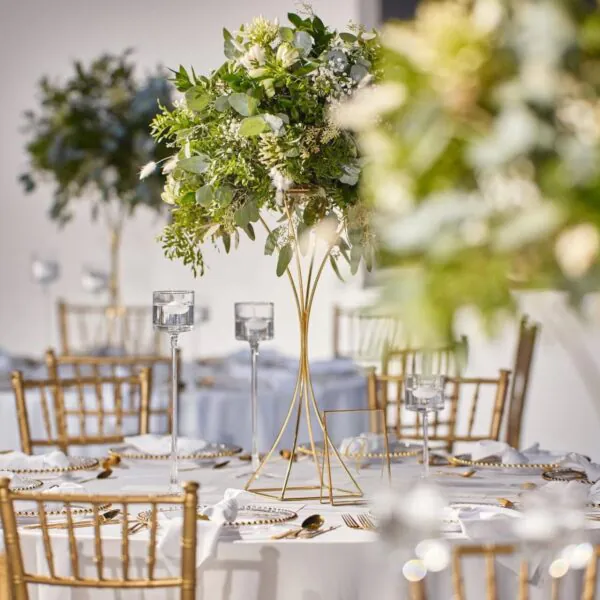 Svadobná výzdoba so zlatými stoličkami a zelenými kvetinovými aranžmánmi v zlatom oblom stojane