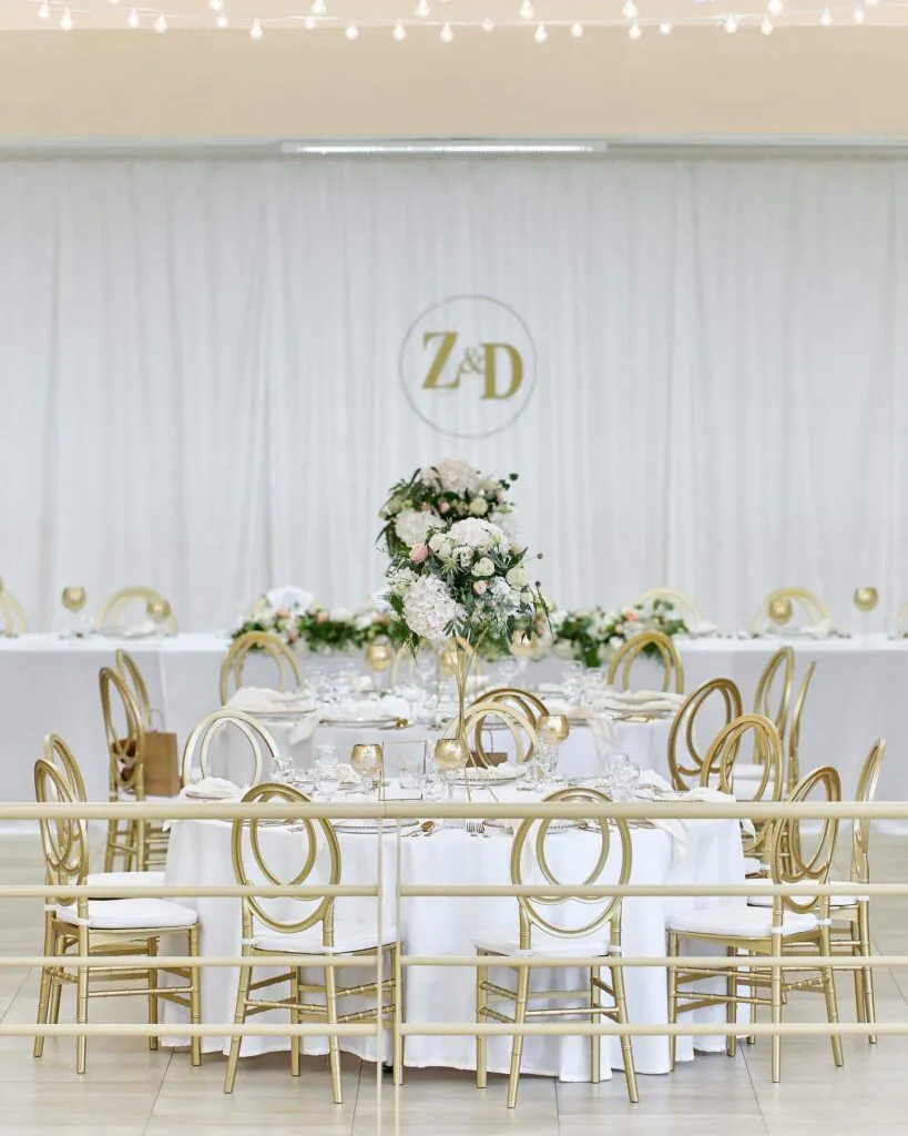 Svadobný stôl so zlatými stoličkami a kvetinovými aranžmánmi KD Šoporňa